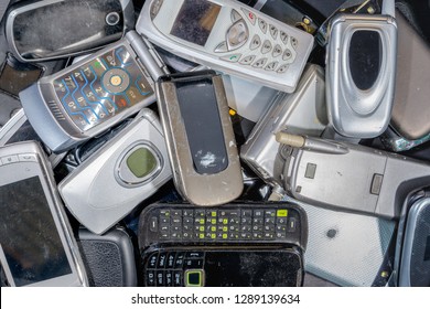 A Pile Of Old Cell Phones To Be Recycled. There Are A Variety Of Phones, But Most Are The Flip To Open Type. The Phones Are Dirty. Branding Was Removed.