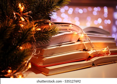 Pile of open books, coniferous branch and garland, closeup