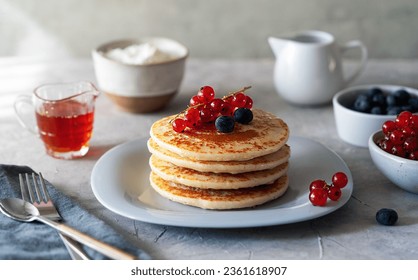 Pile of pancakes with red currants, blueberries, honey, cream cheese, cultery and napkin over grey background - Powered by Shutterstock