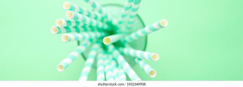 Pile Of Paper Striped White And Green Drinking Straws For Party In Clear Glass Cup On Green Background. Banner