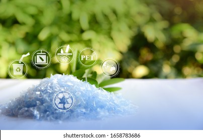 A Pile Of PET Bottle Flakes With Green Tree Blur Background.Recycle Icon,picking Up Plastic Bottle,PET Icon And Compress Bale Icon.Save Environment Concept