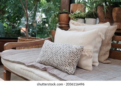 Pile of pillows overlap on wooden chair as living room decoration with green natural garden as background. Contemporary cozy cafe makes people feels like home. Fabric textured pillow is beautiful.