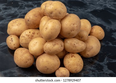 A Pile Of Potatoes On A Black Marble Worktop. 