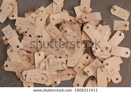 A pile of pricetags with prices on a vintage beige colored paper. Different tags with various numbers and prices laying on a grey background