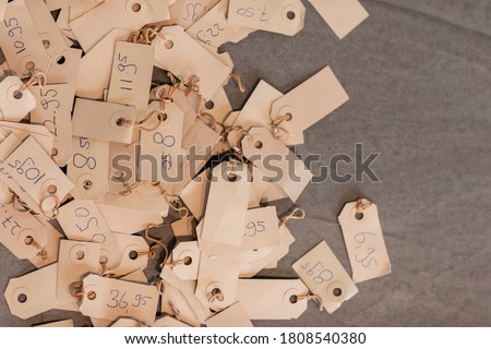 Pile of pricetags with prices on a vintage beige colored paper. Different tags with various numbers and prices laying on a grey background. Empty space on the right