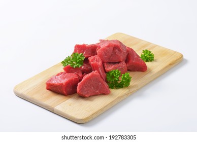 Pile Of Raw Beef Chunks With Fresh Parsley On The Wooden Cutting Board