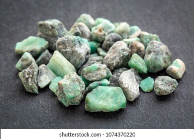 a pile of raw emerald gemstones (mineral beryl) with inclusions mined in Brazil on a gray slate stone - Shutterstock ID 1074370220