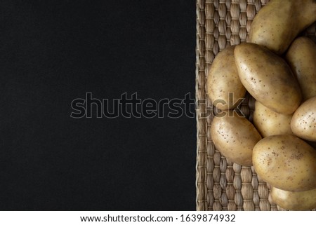 Pile of raw organic potatoes on straw napkin on dark background. Food vegetables groceries from farm with space for text.