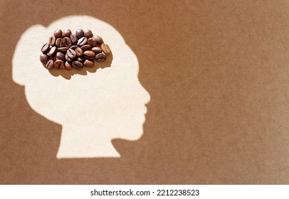 Pile Of Roasted Coffee Beans Arranged Into A Brain Shape Inside A Light Female Head Silhouette On A Craft Paper Background With Copy Space. Caffeine Addiction And Withdrawal Concept.