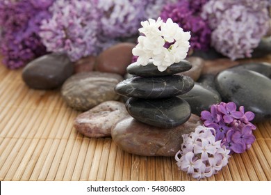 Pile of rocks with flowers on a bamboo mat. Focus on white flower on top of stack.