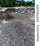 A pile of rocks that have been crushed into small shapes as a mixture when making concrete. Behind it is sand, large rocks and dismantled buildings.