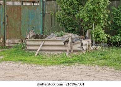 a pile of rubble fenced with pieces of gray slate on the street in green grass near the fence wall
