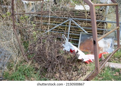 Pile Of Rusting And Broken Farm Gates And Equipment With Grass And Weeds