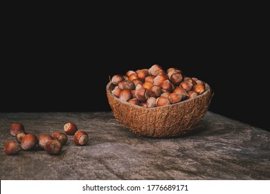 Pile of shelled hazelnuts in a coconut shell bowl on a wooden table on black background. Healthy eating.