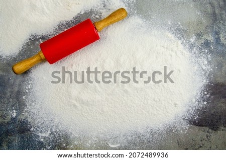 A pile of sifted flour and a rolling pin for rolling out the dough on a dark background of a concrete table top. Sprinkled flour on a cutting board. Space for text. Grainy surface, selective focus.