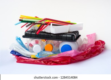 A pile of single use plastic garbage including  water bottles, drinking straws, food packages and carrier bags on white background with copy space. Pollution concept.