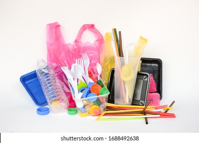 A pile of single use plastic trash including  water bottles, drinking straws, food packages, fork, spoon, caps, cups and carrier bags on white background. Pollution concept.