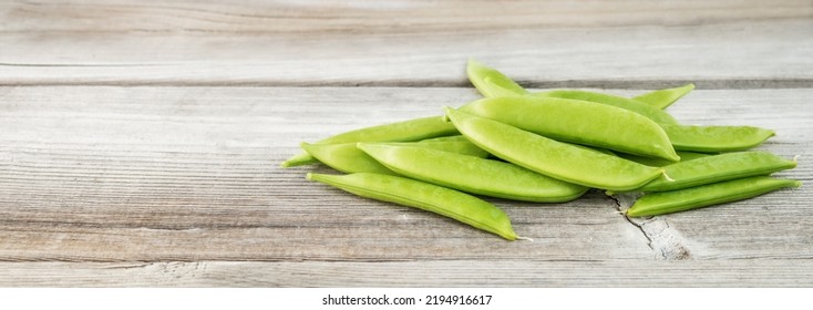 Pile Of Snap Peas On Wood Table. Group Of Fresh Green Pea Pod Shells Just Picked From Garden. Pea Harvest Season From Garden. Sugar Pea, Snap Pea Or Pisum Sativum Var Plant. Selective Focus On Pod.