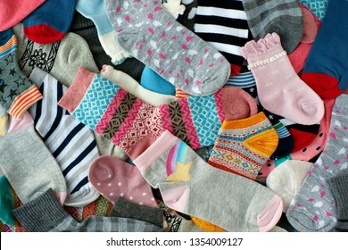 A Pile Of Socks Of Different Colors. Many Socks Of Different Colors And Sizes Create A Background. View From Above. Knitted Clothing In The Form Of Socks.