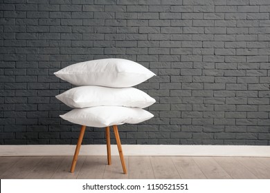 Pile of soft bed pillows on chair near brick wall with space for text