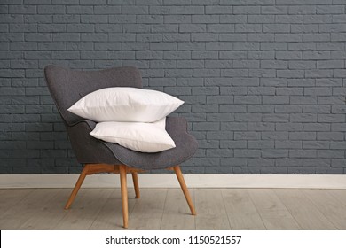 Pile of soft bed pillows on armchair near brick wall with space for text