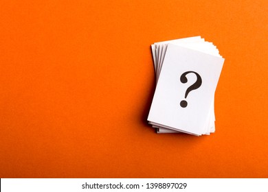Pile of stacked question marks printed on sheets of white paper or signs arranged to the side on a orange background with copy space in a conceptual image.