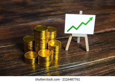 A pile of stacks of coins and an easel with a chart up arrow. Growth in savings and property assets. Enrichment and wealth. Successful investment. Accumulation of pension Funds. Deposit banking. - Shutterstock ID 2126487761