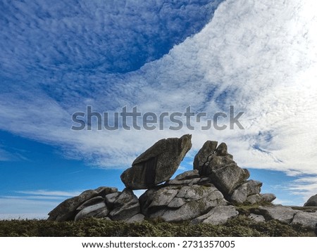 Pile of stones under a dramatic cloud-filled sky, set in a natural landscape with rugged terrain.