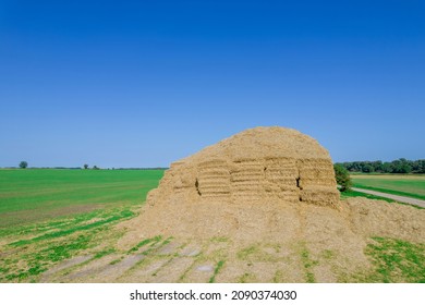 Pile of straw in bales in the middle of a field near a field road.