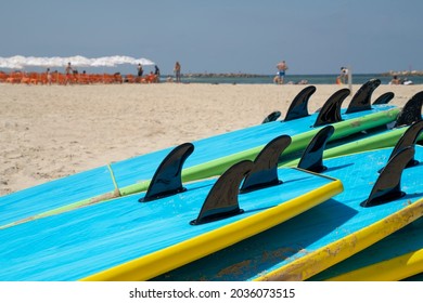 A pile of surfboards on a sandy beach in Tel Aviv, Israel, on a sunny day. Bathers in the background. - Powered by Shutterstock