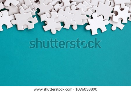 A pile of uncombed elements of a white jigsaw puzzle lies on the background of a blue surface. Texture photo with copy space for text