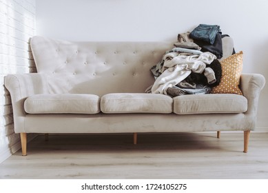 Pile of unfolded clothes for laundry on scandinavian grey sofa. Heap of used clothes for donation and recycling. Concept of minimalism, simplicity and spring wardrobe cleaning. Decluttering home
