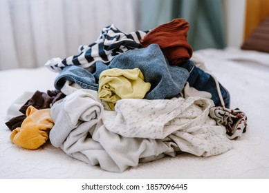 Pile of unfolded dirty clothes for laundry on the bed. Heap of used clothes for donation and recycling. Concept of minimalism, declutter, mess and wardrobe cleaning
