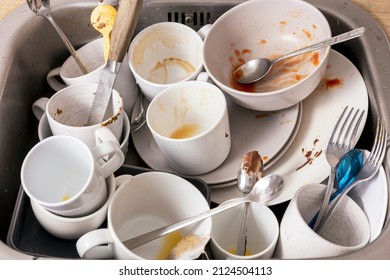 Pile of unwashed, dirty dishes in the sink. Mess in the kitchen. Dirty kitchenware, plates and mugs. Chaos at home. Laziness. Cluttered apartment. Messy cutlery and dishware.