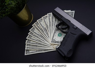 Pile Of US Dollar Cash And A Black Gun. Viewed From Above On A Black Table.