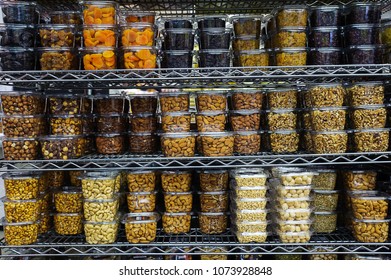 Pile Of Various Dried Fruit And Nuts Packaged In Airtight Transparent Plastic Containers For Convenience And Freshness, Positioned On A Metal Rack Or Shelf At The Supermarket 