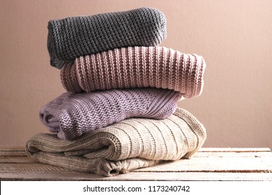 A pile of warm sweaters on a wooden table on a light background. Autumn and winter clothes.
