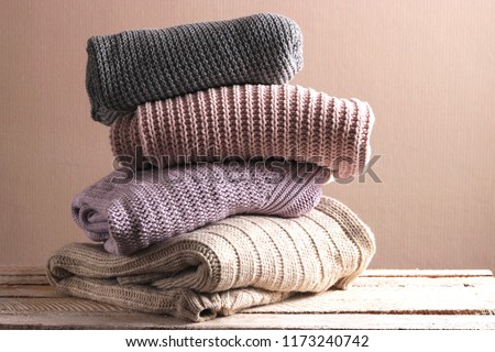 A pile of warm sweaters on a wooden table on a light background. Autumn and winter clothes.
