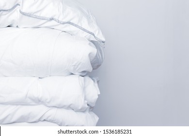 Pile of white bedding items, pillows and a blanket on white background with copy space