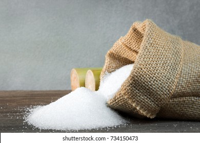 Pile of white sugar in an open and overturned sack with sugar cane, With copy space for your text message or promotional content.