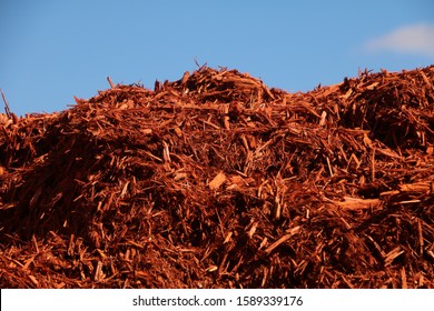 Pile Of Wood Mulch In Sun With Blue Sky Behind And Shadows.