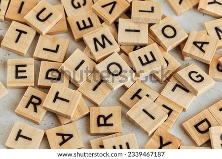 Pile of wooden tiles with various letters scattered on white stone like board, closeup view from above