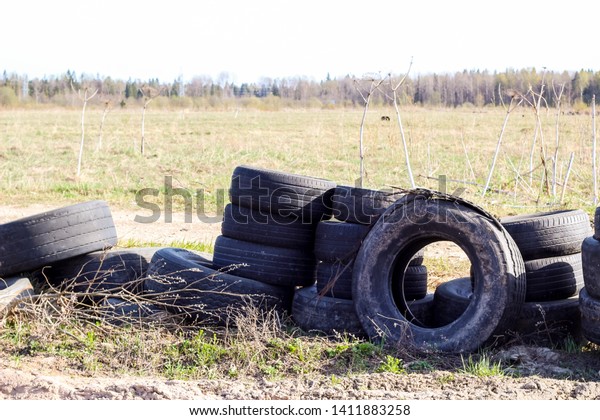 A pile of\
worn car tires dumped on the field. Environmental pollution.\
Landfill of used tires, car waste. Car waste recycling, automotive\
industry. Rubbish along the\
road