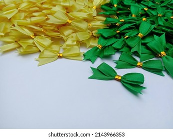 Pile of yellow and green satin ribbon bow ties isolated on white background. Sticky tape for souvenirs, handmade. Focus on foreground.