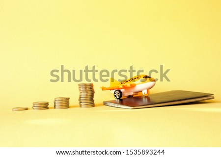 Piles of coins are laid out in increasing number of coins in a stack on a yellow background and an orange plane with a passport. Concept - money for travel, the cost of a flight, travel accumulation.