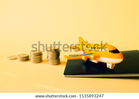 Piles of coins are laid out in increasing number of coins in a stack on a yellow background and an orange plane with a passport. Concept - money for travel, the cost of a flight, travel accumulation.