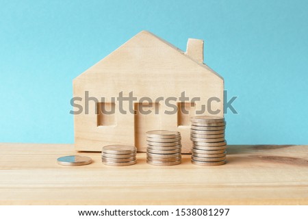 Piles of coins and a wooden  house on a blue background. Concept - real estate investment, family budget or money to pay rent or purchase a home.