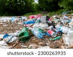 Piles of garbage in the forest, random dumping in nature. Stink heap, plastic bag and bottles, rubbish in polluted green  grass of nature landscape background. The concept of human pollution of forest