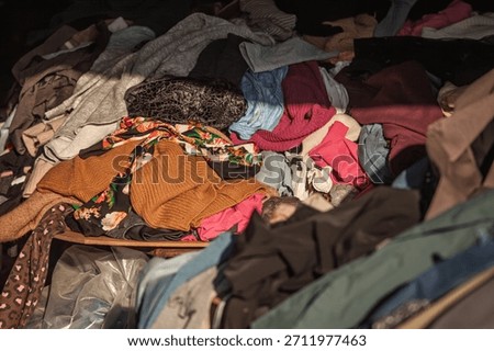 Piles of second hand clothes in a flea market, with mixed garments and colors in a casual heap. The scene evokes thrift shopping, resale, and the circular economy in everyday fashion.