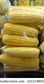 Piles Of Sweetcorn Wrapped In Plastic For Sale In Supermarket. Sweet Corn (Zea Mays Saccharata Group) Is One Of The Most Important Commercial Maize Cultivationcultivar Group.